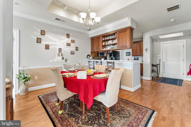 dining space featuring crown molding, a tray ceiling, light hardwood / wood-style floors, and a notable chandelier