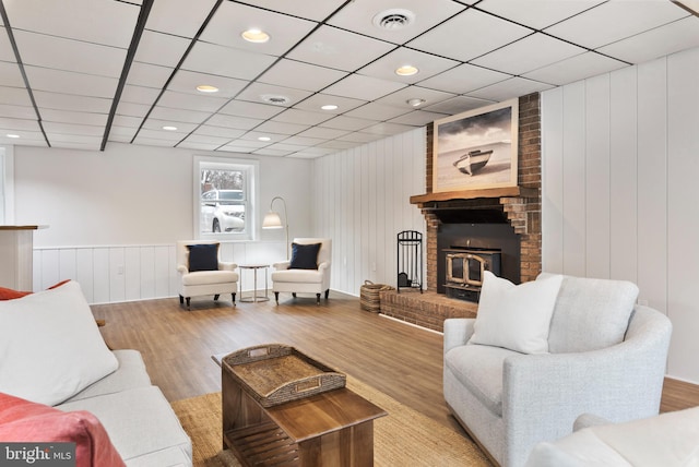 living room featuring a brick fireplace, a drop ceiling, and light hardwood / wood-style floors