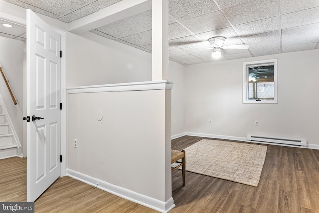 basement featuring a baseboard heating unit, a drop ceiling, and dark hardwood / wood-style flooring