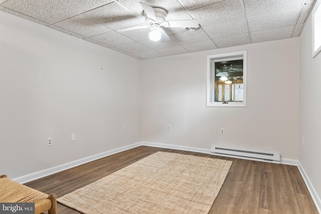 spare room with a baseboard radiator, dark hardwood / wood-style floors, a drop ceiling, and ceiling fan