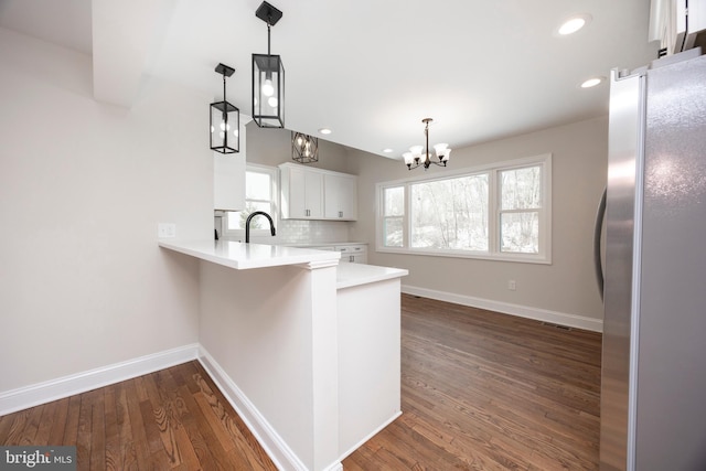 kitchen with stainless steel refrigerator, white cabinetry, hanging light fixtures, decorative backsplash, and kitchen peninsula