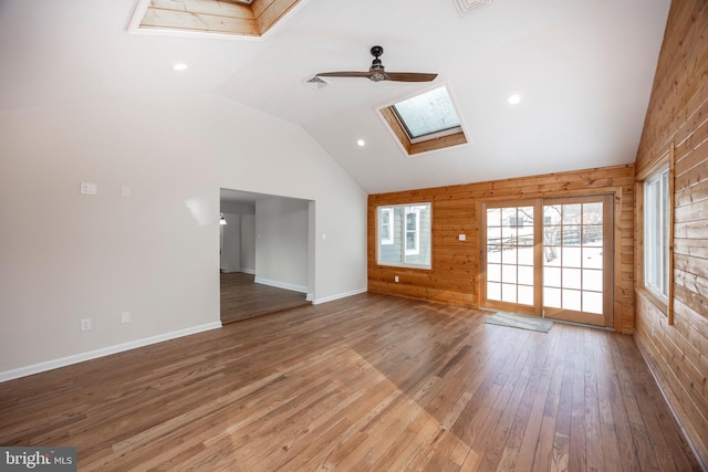 unfurnished living room featuring ceiling fan, wood-type flooring, vaulted ceiling with skylight, and wood walls