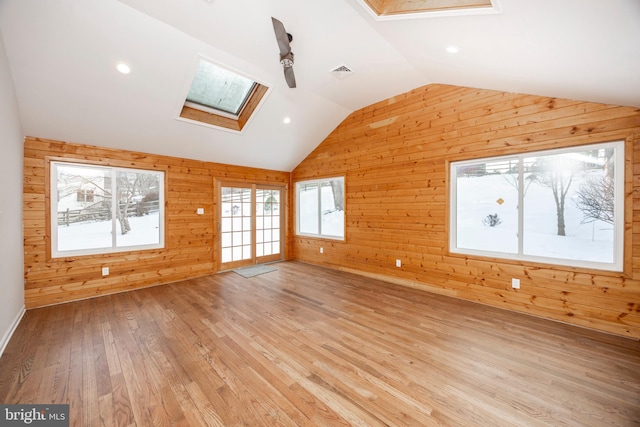 additional living space featuring ceiling fan, wooden walls, light hardwood / wood-style floors, and vaulted ceiling with skylight