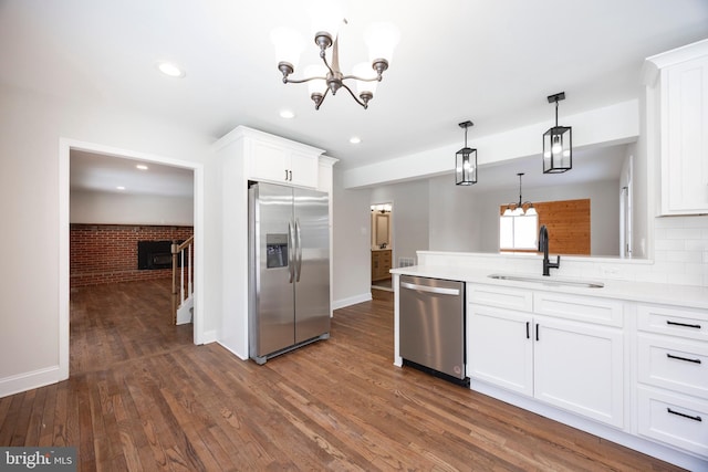 kitchen with sink, hanging light fixtures, appliances with stainless steel finishes, brick wall, and white cabinets