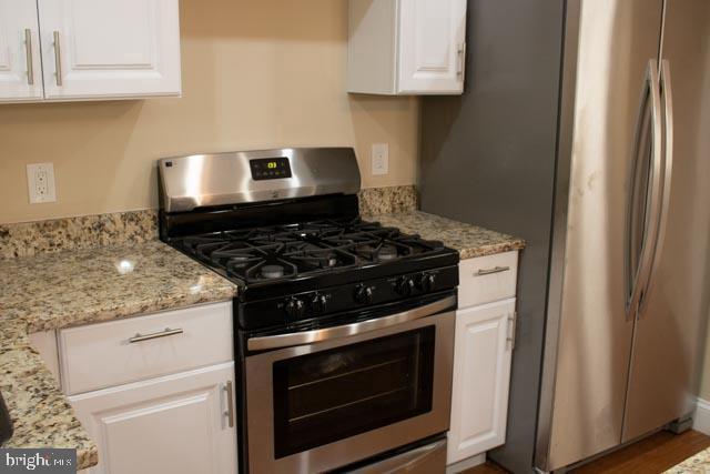 kitchen featuring light stone countertops, stainless steel appliances, and white cabinetry