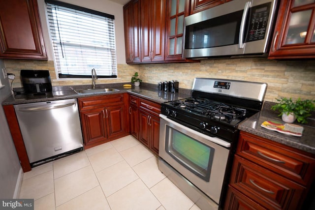 kitchen with appliances with stainless steel finishes, dark stone counters, decorative backsplash, sink, and light tile patterned floors