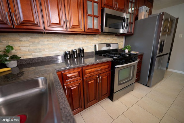 kitchen with light tile patterned floors, appliances with stainless steel finishes, tasteful backsplash, and dark stone countertops