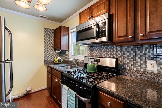 kitchen with appliances with stainless steel finishes, dark hardwood / wood-style floors, dark stone counters, ornamental molding, and sink