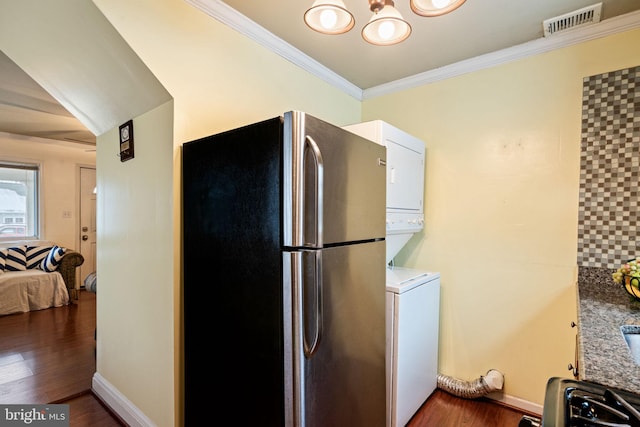 kitchen with dark wood-type flooring, stacked washer / drying machine, stainless steel fridge, and crown molding