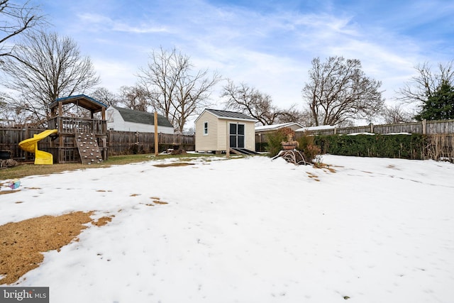 snowy yard with a playground and a shed