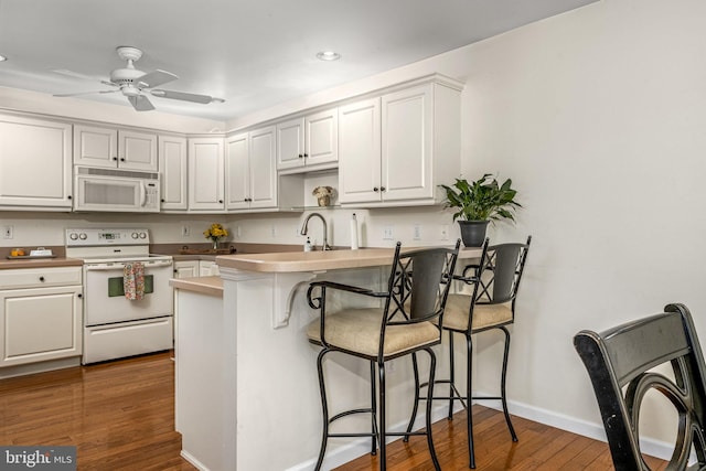 kitchen featuring a kitchen bar, white cabinetry, kitchen peninsula, white appliances, and hardwood / wood-style floors