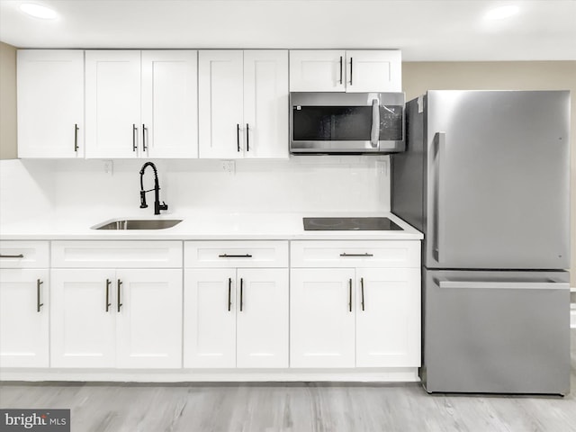 kitchen with light hardwood / wood-style flooring, sink, white cabinets, tasteful backsplash, and stainless steel appliances