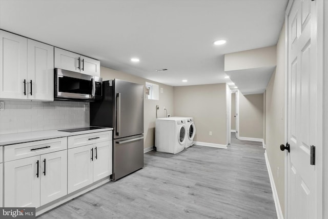 kitchen with white cabinetry, light wood-type flooring, backsplash, washing machine and dryer, and stainless steel appliances