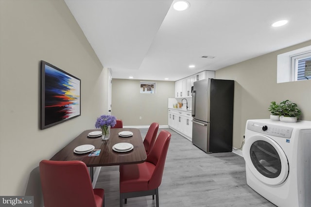 interior space with light hardwood / wood-style floors, washer / clothes dryer, white cabinets, sink, and stainless steel fridge