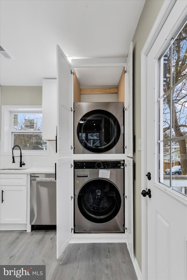 laundry room featuring sink, light wood-type flooring, a wealth of natural light, and stacked washer and dryer