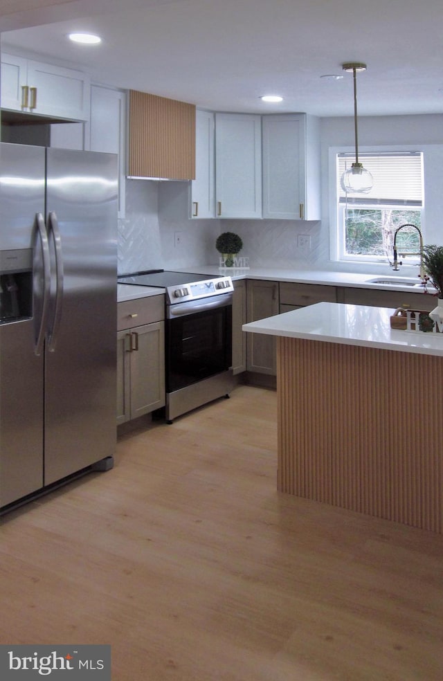 kitchen with tasteful backsplash, sink, decorative light fixtures, light hardwood / wood-style flooring, and stainless steel appliances