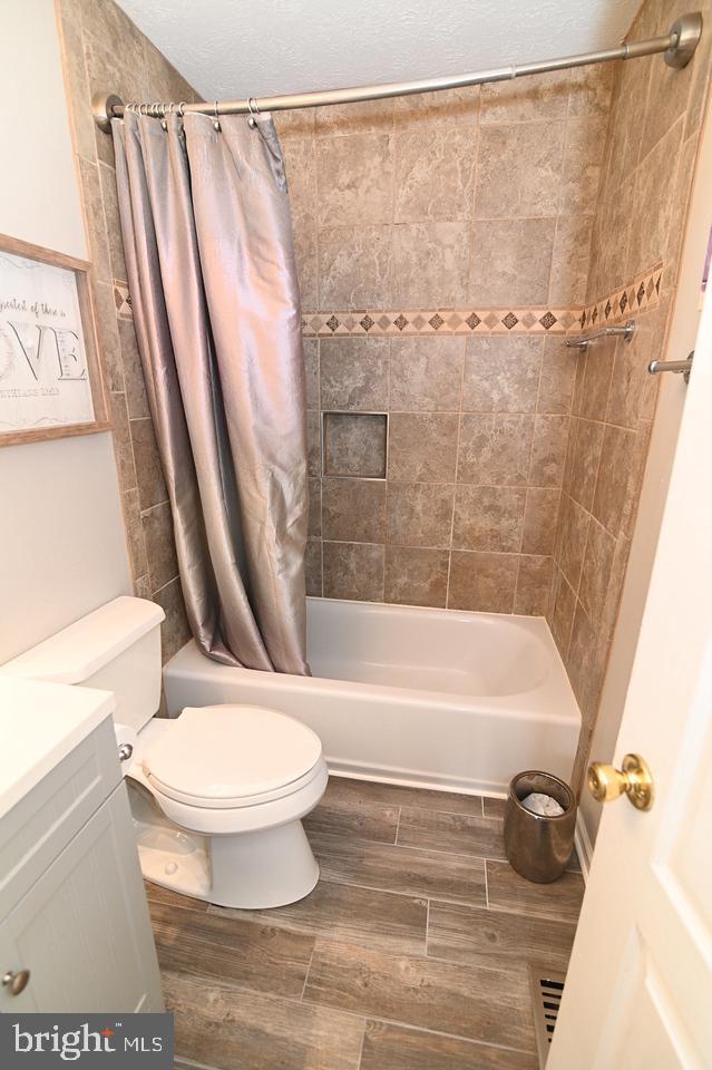 full bathroom featuring toilet, vanity, shower / tub combo with curtain, and a textured ceiling