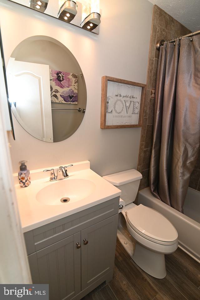 full bathroom featuring hardwood / wood-style floors, a textured ceiling, vanity, toilet, and shower / bath combo with shower curtain