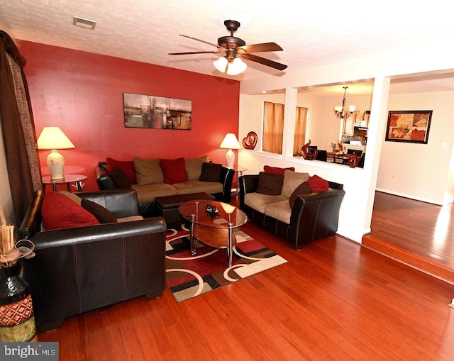 living room featuring wood-type flooring, ceiling fan with notable chandelier, and a textured ceiling