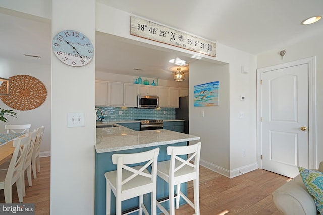 kitchen with kitchen peninsula, sink, tasteful backsplash, a breakfast bar, and stainless steel appliances