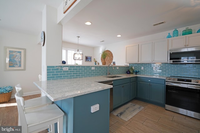 kitchen featuring decorative light fixtures, stainless steel appliances, sink, kitchen peninsula, and light stone counters