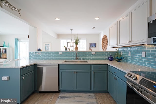 kitchen featuring kitchen peninsula, hanging light fixtures, sink, blue cabinets, and stainless steel appliances