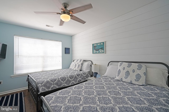 bedroom with ceiling fan, wood walls, dark wood-type flooring, and multiple windows