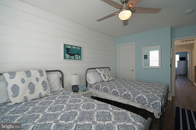 bedroom with ceiling fan, dark wood-type flooring, and wooden walls