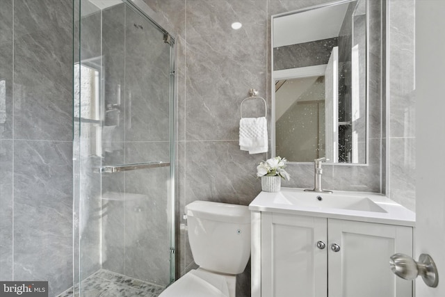 bathroom with vanity, toilet, a shower with shower door, and tile walls