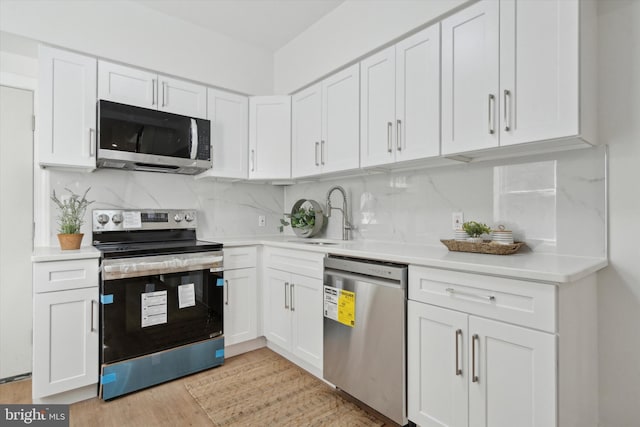 kitchen with sink, stainless steel appliances, tasteful backsplash, white cabinets, and light wood-type flooring