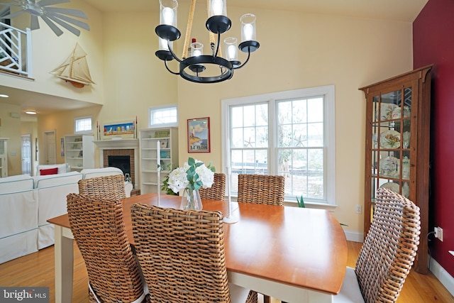 dining room featuring a towering ceiling, a fireplace, and light hardwood / wood-style floors