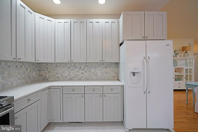 kitchen featuring light stone counters, stainless steel range, white refrigerator with ice dispenser, and decorative backsplash