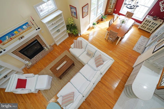 living room featuring a brick fireplace, hardwood / wood-style flooring, a wealth of natural light, and a notable chandelier