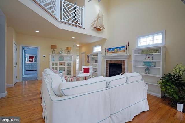 living room featuring a brick fireplace, light hardwood / wood-style flooring, and a high ceiling