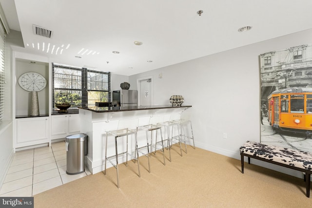 kitchen with white cabinetry, a breakfast bar, stainless steel refrigerator, and kitchen peninsula