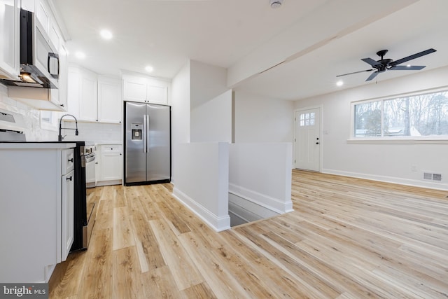 kitchen with ceiling fan, backsplash, light wood-type flooring, appliances with stainless steel finishes, and white cabinets