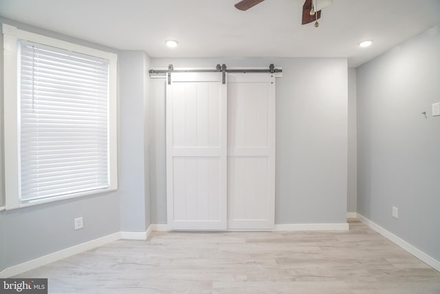 unfurnished bedroom featuring ceiling fan, light hardwood / wood-style floors, multiple windows, and a barn door