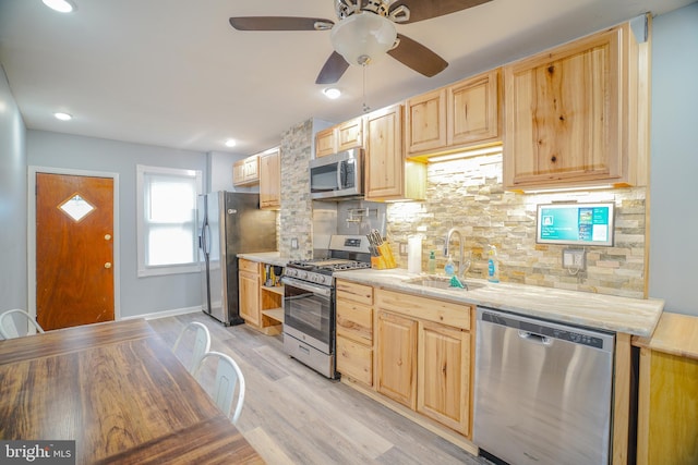 kitchen featuring appliances with stainless steel finishes, light brown cabinets, sink, backsplash, and light wood-type flooring