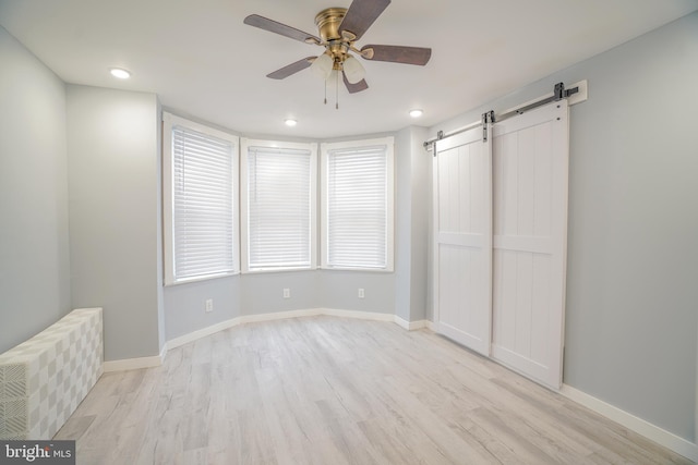 unfurnished bedroom with light wood-type flooring, ceiling fan, a closet, and a barn door