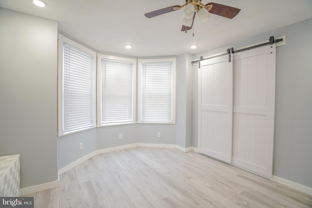 unfurnished bedroom featuring light wood-type flooring, ceiling fan, and a barn door