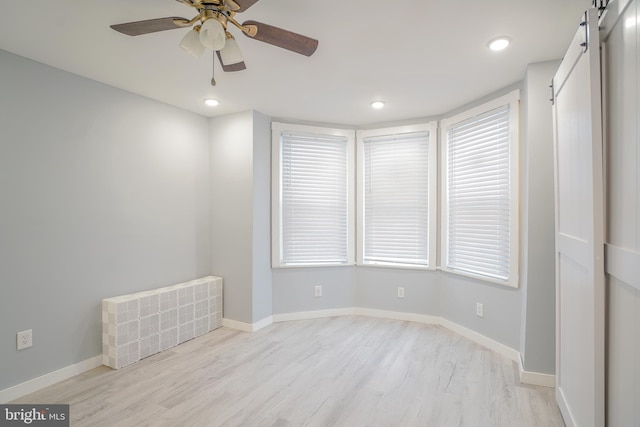 empty room with ceiling fan, a wealth of natural light, light hardwood / wood-style flooring, and a barn door