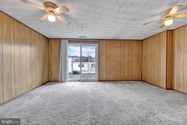 empty room with ceiling fan, light colored carpet, and wood walls