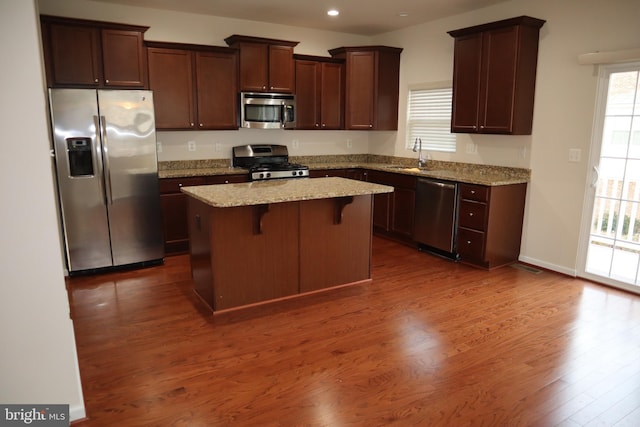 kitchen with sink, stainless steel appliances, a kitchen breakfast bar, light stone countertops, and a kitchen island