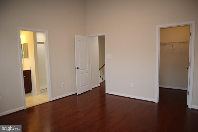 unfurnished bedroom with a walk in closet, ensuite bathroom, dark hardwood / wood-style floors, and a closet