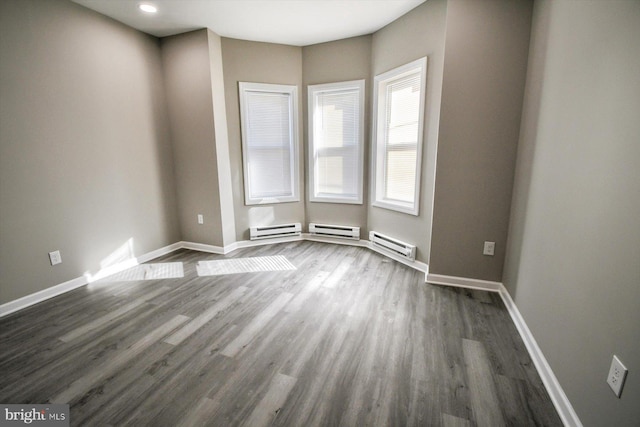 empty room with dark wood-type flooring and a baseboard heating unit