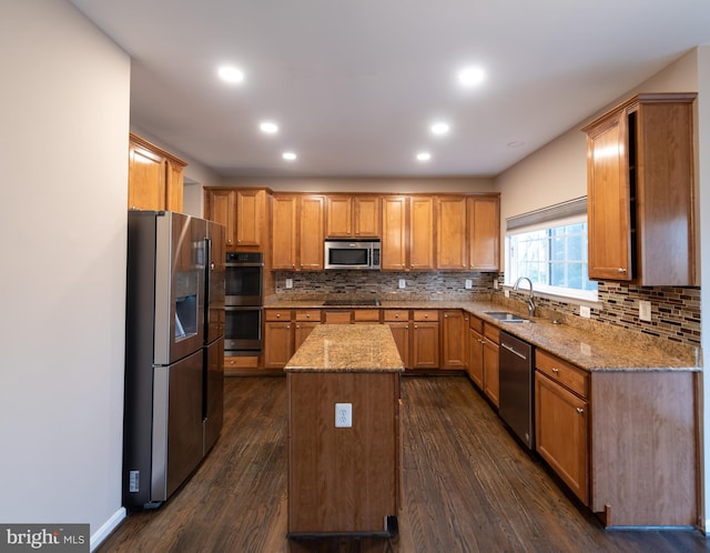 kitchen with stainless steel appliances, light stone countertops, a kitchen island, and sink