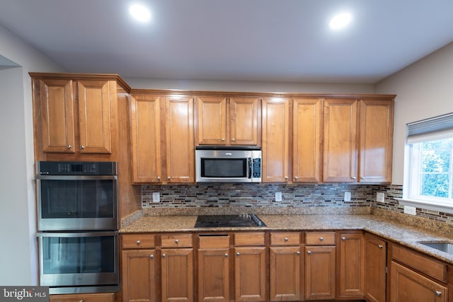 kitchen with tasteful backsplash, appliances with stainless steel finishes, sink, and light stone counters