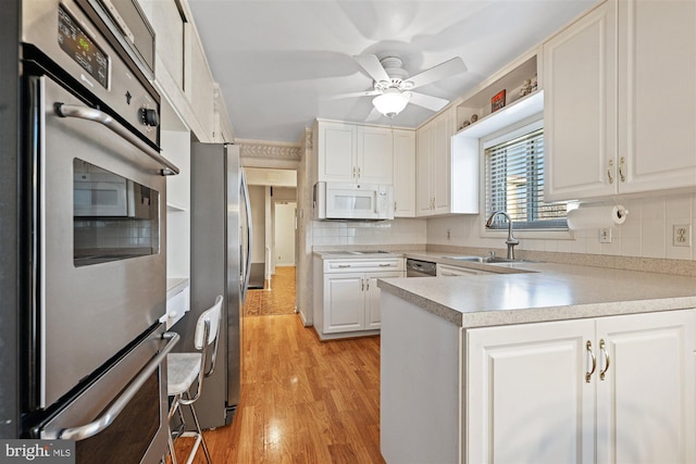 kitchen featuring appliances with stainless steel finishes, a sink, light countertops, white cabinetry, and backsplash