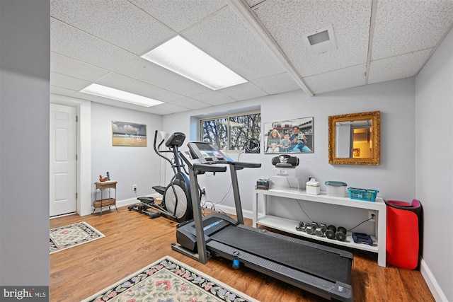 exercise room with a paneled ceiling, wood finished floors, visible vents, and baseboards