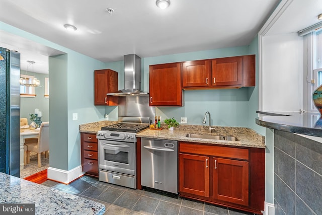 kitchen featuring light stone countertops, sink, pendant lighting, stainless steel appliances, and wall chimney exhaust hood